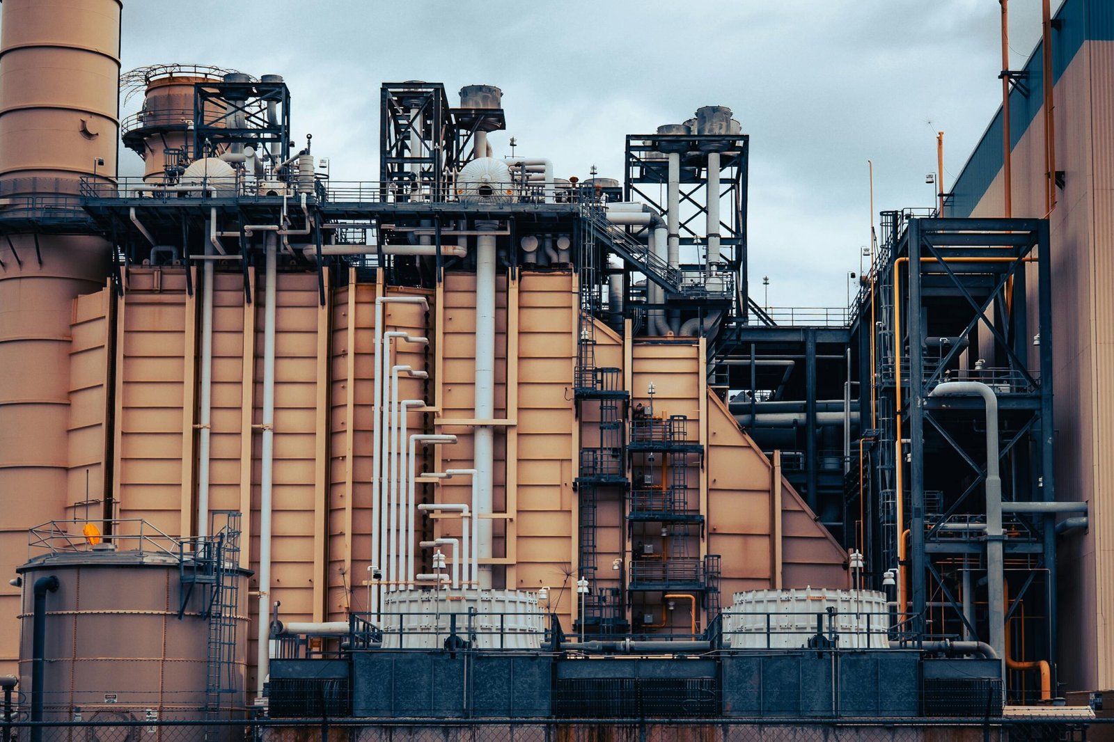 Detailed view of an industrial factory's exterior, showcasing machinery and structures under a cloudy sky.