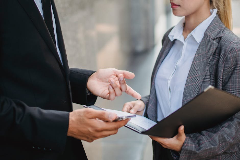 A businessman and businesswoman in formal attire engage in a focused discussion outdoors.