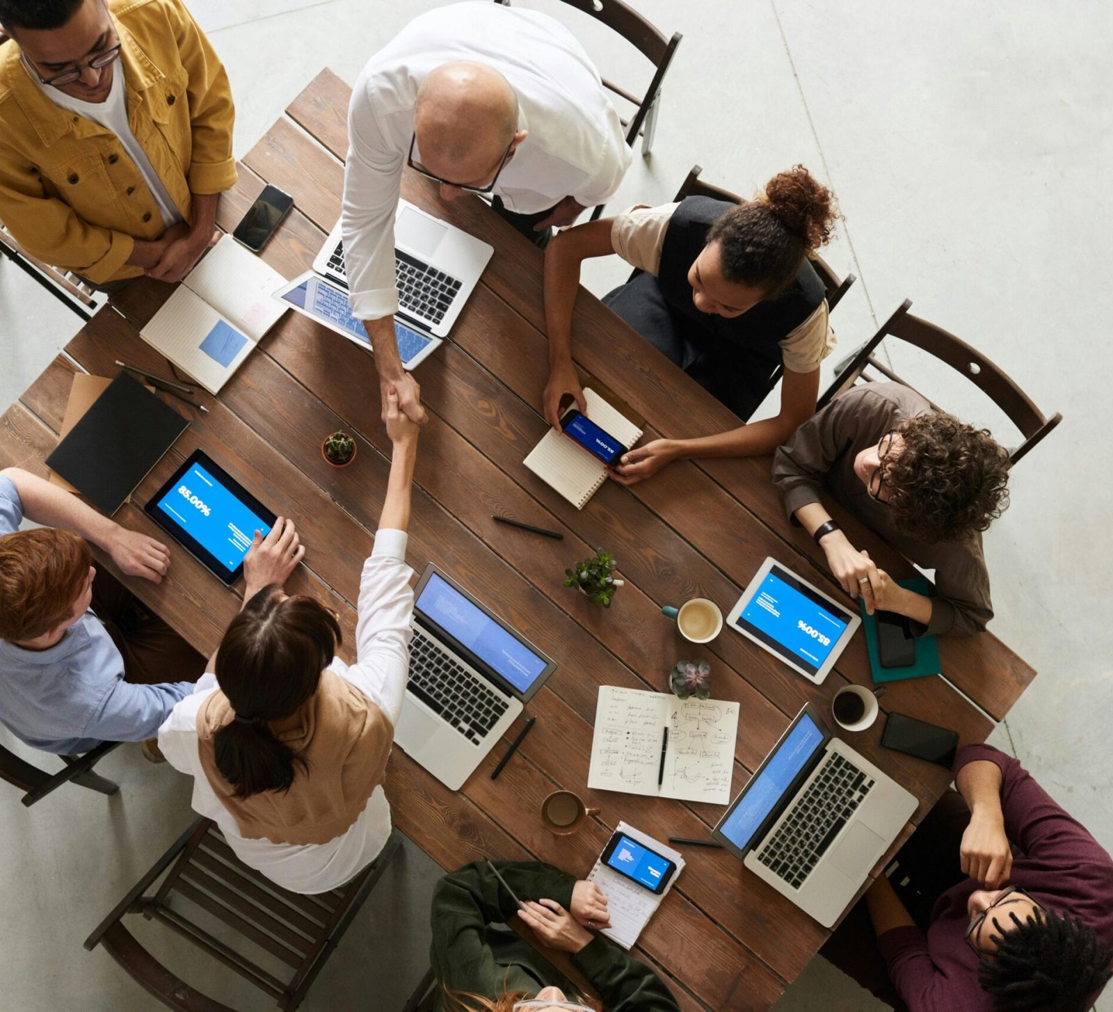 Top view of a diverse team collaborating in an office setting with laptops and tablets, promoting cooperation.