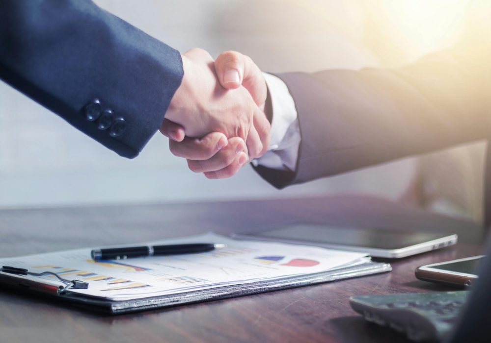 Professional handshake agreement over business charts in an office setting.