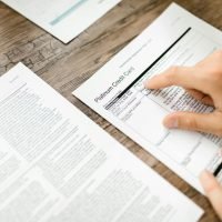 A hand examining a credit card agreement on a wooden desk, highlighting financial review.