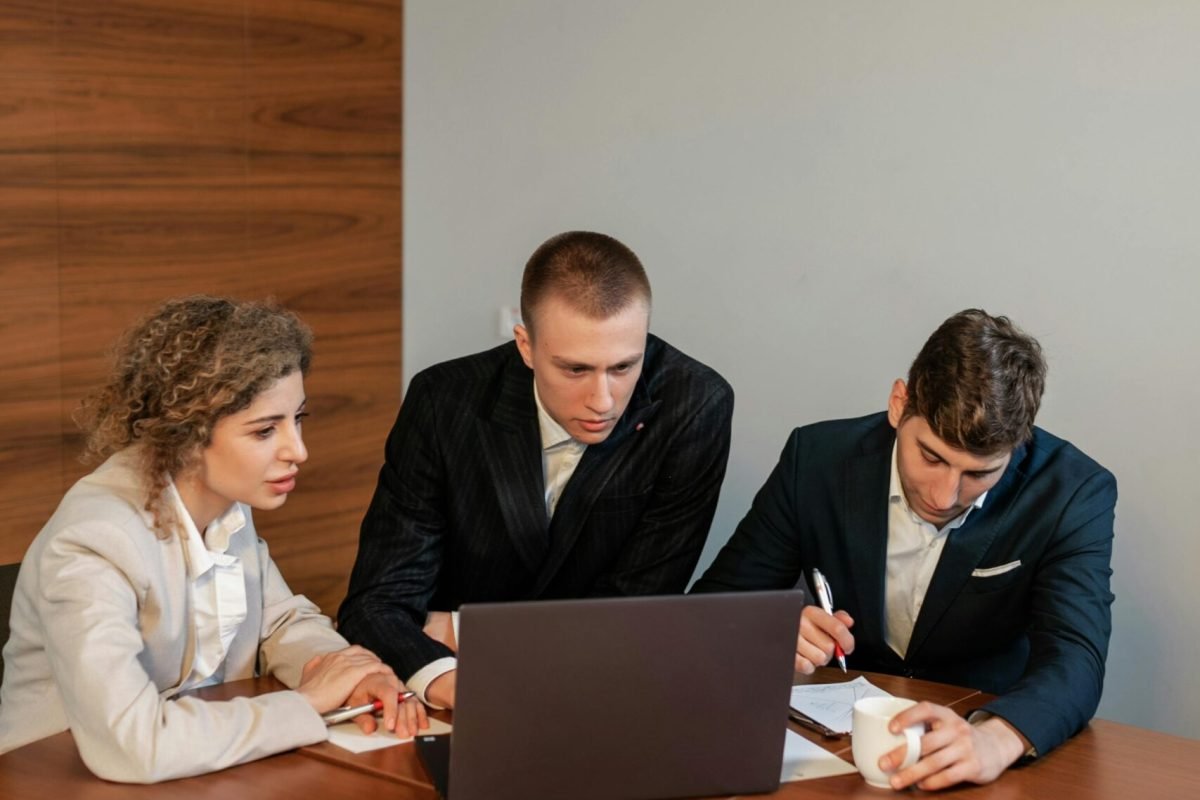 Collaborative business meeting with three professionals focused on a laptop in a modern office.
